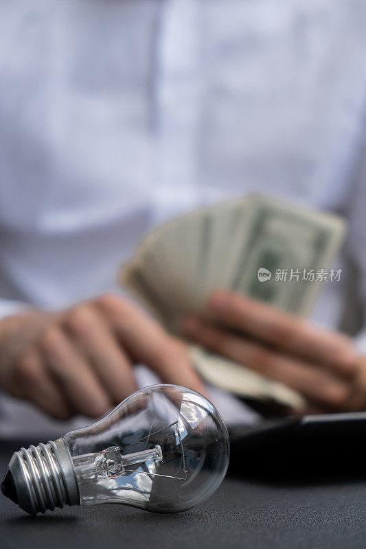 Electric light bulb. Man hands counting expenses bills on electricity banknotes of dollar cash accounting on calculator. Close up of hands unrecognizable Businessman. High prices for energy. Save up budget investment concept Planning budget and estimating